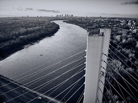 Beautiful panoramic aerial drone view to cable-stayed Siekierkowski Bridge over the Vistula river and Warsaw City skyscrapers, Poland in gold red autumn colors in November evening at sunsetの写真素材