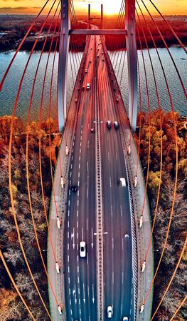 Beautiful panoramic aerial drone view to cable-stayed Siekierkowski Bridge over the Vistula river and Warsaw City skyscrapers, Poland in gold red autumn colors in November evening at sunsetの写真素材