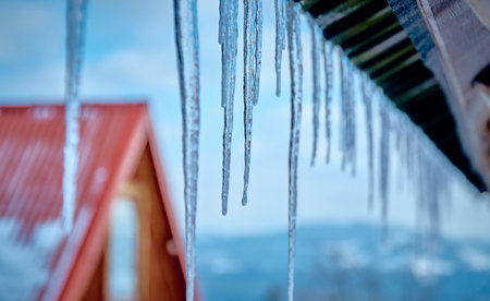 Strong real winter in the south of Poland - huge icicles hanging from the roof against the blue sunny skyの写真素材