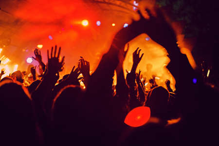 Abstract blur atmosphere: happy people enjoying outdoor music festival concert, raised up hands and clapping of pleasure, active night life concept, play of light and shadow on the huge stageの写真素材