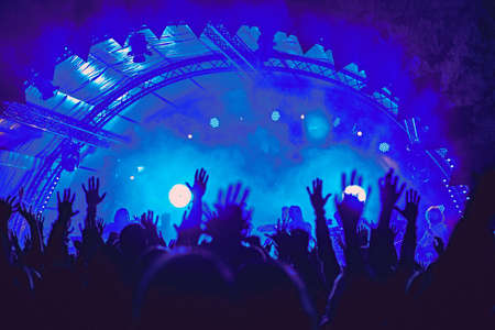 Abstract blur atmosphere: happy people enjoying outdoor music festival concert, raised up hands and clapping of pleasure, active night life concept, play of light and shadow on the huge stageの写真素材