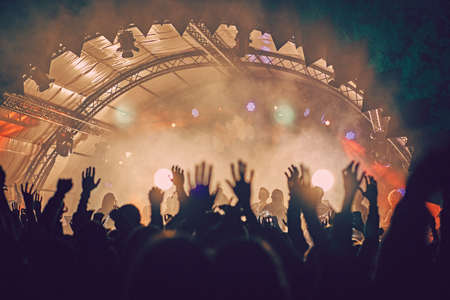 Abstract blur atmosphere: happy people enjoying outdoor music festival concert, raised up hands and clapping of pleasure, active night life concept, play of light and shadow on the huge stageの写真素材