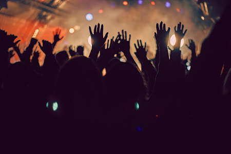 Abstract blur atmosphere: happy people enjoying outdoor music festival concert, raised up hands and clapping of pleasure, active night life concept, play of light and shadow on the huge stageの写真素材