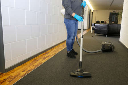 Office cleaning: Cleaner vacuums the corridor of an officeの写真素材
