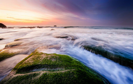 sunset seascape with rocks covered by green moss and waves trails. Photo taken at Kudat, Sabah...