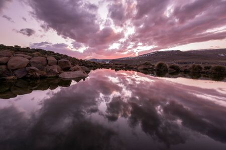 A beautiful early evening photograph of a lake in the snow covered mountains of the Lesotho Highlands. The pink stormy clouds create incredible reflections in the water.の写真素材