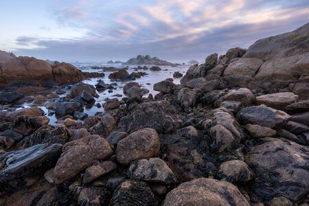 A beautiful misty seascape at sunrise with clouds in the dramatic sky, with large rocks in the foreground, taken at Paternoster, South Africa.の写真素材