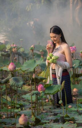 A beautiful woman in traditional Thai northern traditional costume stand in pink lotus pond , identity culture of Thailand.の写真素材