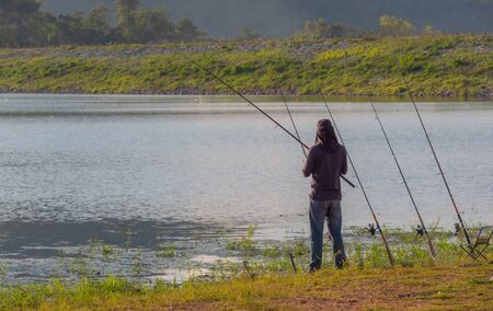 Fisherman fishing with a fishing rod. Silhouette. Trees and cottages in the background reservoir.の写真素材