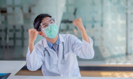 Handsome male doctor sat on the table and raised his hand to show joy.の写真素材