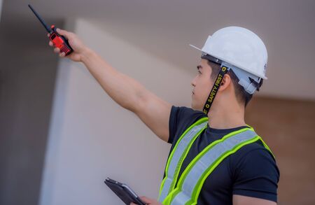 Strong foreman wearing a white helmet, holding a radio communication and a tablet on the construction site.の写真素材