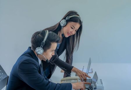 How can I help you? Beautiful call center employees in headphones are working at modern offices, focusing on woman.How can I help you? Beautiful call center employees in headphones are working at modern offices, focusing on women.の写真素材