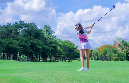 Woman golf player in action being setup address of back swing to hit the golf ball away from T-OFF to the destination on the green, fairway at day light sky.の写真素材