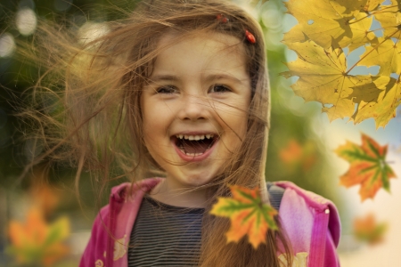 little girl in autumn with falling leaves and hair in wind の写真素材