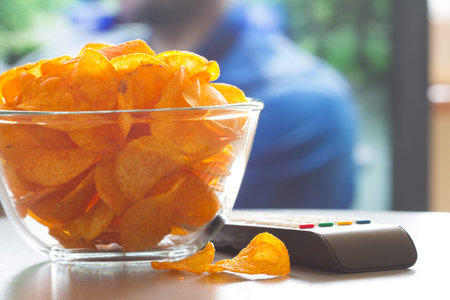 Bowl of chips, remote control and background television. Home cinema concept