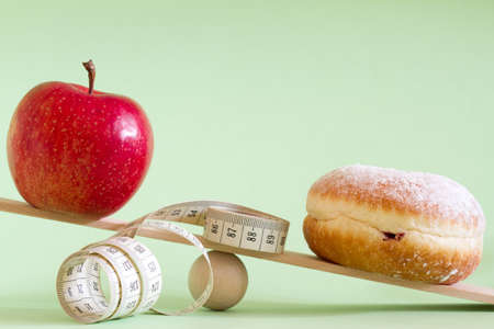Apple and donut with a tape measure on wooden seesaw, healthy lifestyle conceptの写真素材