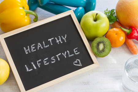 Words HEALTHY LIFESTYLE on chalkboard. Fruits, vegetables and dumbbells, healthy diet and sport conceptの写真素材