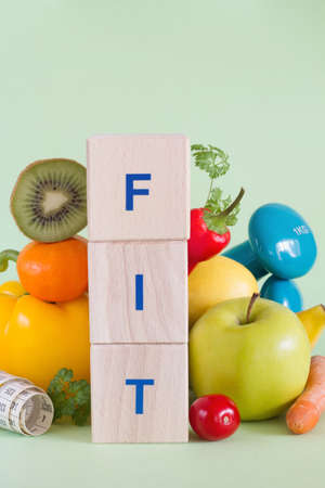 Word FIT made with wooden blocks. Fruits, vegetables, measuring tape and dumbbells, healthy food and lifestyle conceptの写真素材