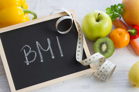 Word BMI on chalkboard. Fruits, vegetables and measuring tape, healthy diet conceptの写真素材