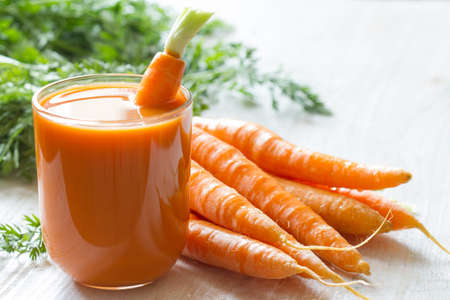 Healthy fresh carrot juice in glass on white wooden tableの写真素材