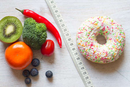 Donut vs. fruits and vegetables on white wooden background and tape measure, diet and calories conceptの写真素材