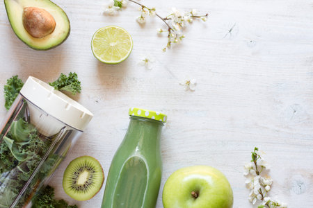 Spring green smoothie in glass bottle with composition of fruits and flower on light backgroundの写真素材