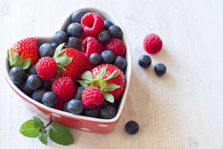 Fresh blueberries, raspberries and strawberries in heart shaped bowlの写真素材