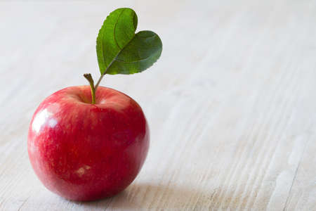 Red apple with heart-shaped leaf on light backgroundの写真素材