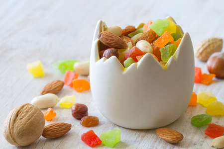 Mix of nuts and candied fruits in eggshell shaped bowl on light background, easter baking conceptの写真素材