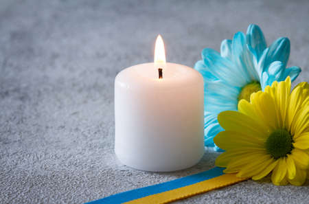 Burning candle, ribbon and flowers in colors of Ukrainian flag, memory of victims in Ukraine conceptの写真素材