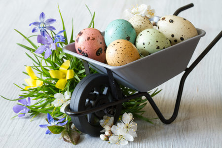 Colored eggs on wheelbarrow, grass and spring flowers, easter decoration concept