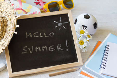 Lettering hello summer on chalkboard with school notebooks, ball, flowers and summer accessories, summer vacation conceptの写真素材