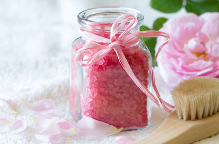 Rose bath salt in glass bottle, body care accessories and fresh rose petals on light background, spa conceptの写真素材