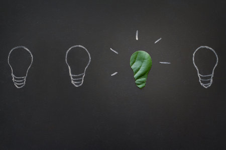 Light bulbs drawn on chalkboard and light bulb made with green leaf, concept of environmental protection and ecologyの写真素材