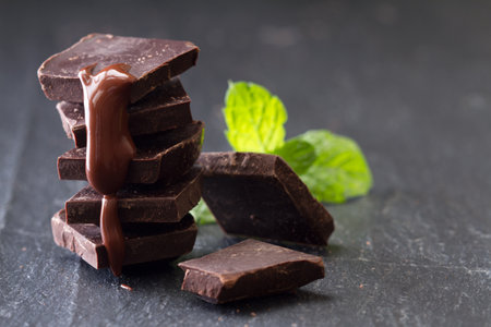A few cubes of dark chocolate with mint leaves and chocolate sauce on black backgroundの写真素材