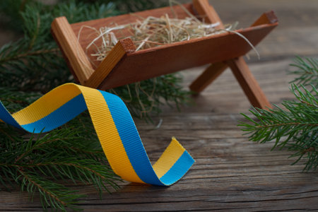 Manger of Jesus with christmas tree branches and ribbon in colors of ukrainian flag, symbol of hope conceptの写真素材
