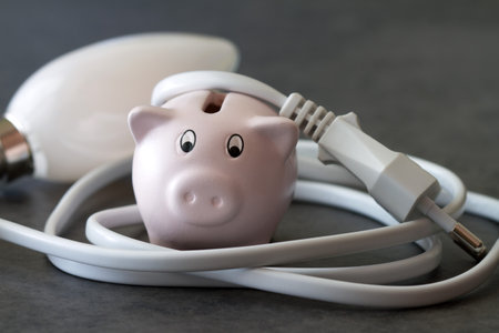 Piggy bank wrapped with cable, concept of rising electricity pricesの写真素材