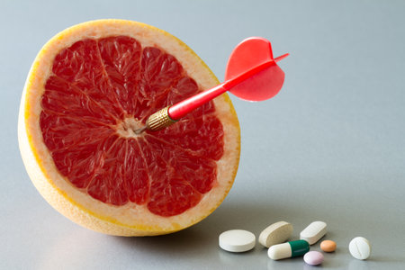 Aiming red dart at center of grapefruit and pile of pills, healthy diet vs medicine, creative concept of choosing synthetic vitamins or natural fruitsの写真素材