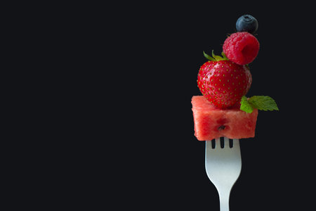 Summer fresh fruits on fork, black background with copy space, creative concept