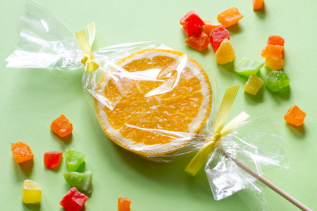 Orange slice on stick wrapped in foil and candied fruit, fruit lollipop, healthy substitute for sweets, creative conceptの写真素材