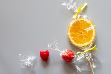 Orange slice on stick and fruits wrapped in foil, fruit lollipop, candies, healthy substitute for sweets, creative conceptの写真素材