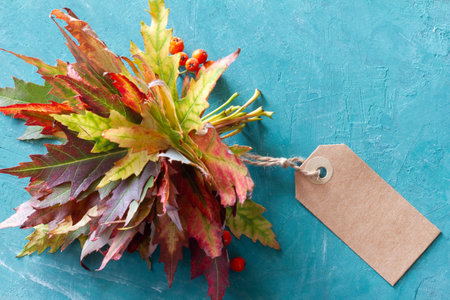 Autumn bouquet of leaves with blank tag on turquoise background