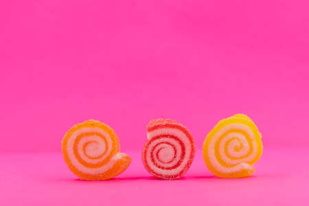 Closed up three spiral shape jelly candy, yellow red orange roll with sugar surface, pastel bright pink backgroundの写真素材