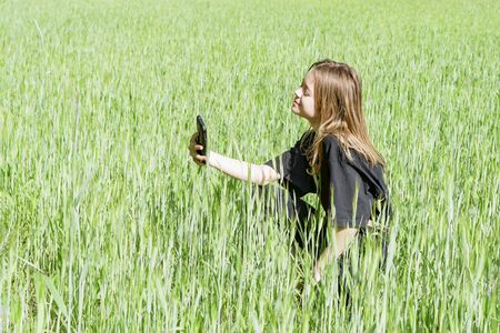 A young girl takes photos of herself in a sown field on her mobile phoneの写真素材