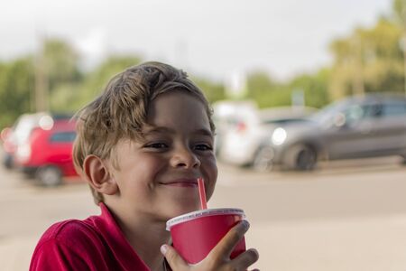 A little boy is sitting in a summer cafe and drinking a refreshing drinkの写真素材