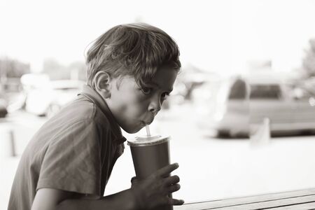 A little boy is sitting in a summer cafe and drinking a refreshing drinkの写真素材