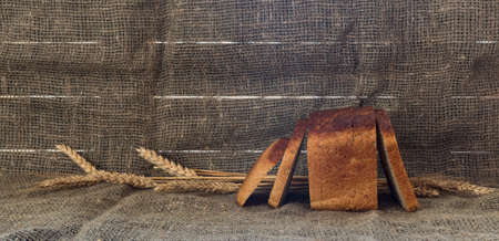A sliced loaf of black bread on a dark burlap backgroundの写真素材