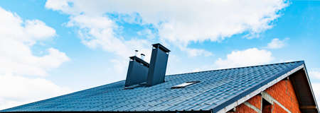 A fragment of a metal roof with a chimney and a window in a new house under constructionの写真素材