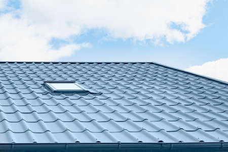 A fragment of a metal roof with a chimney and a window in a new house under constructionの写真素材