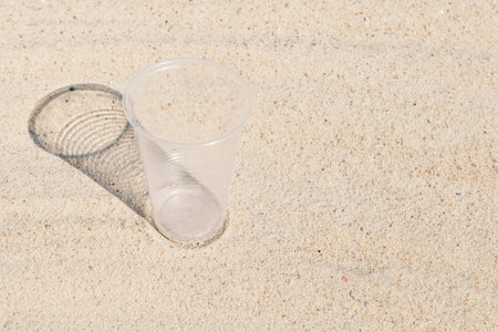 A clear plastic Cup stands on the hot river sand